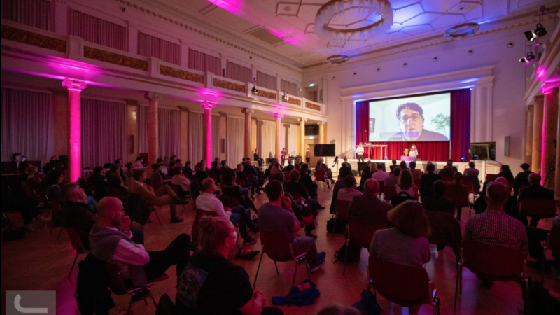 SILBERSALZ Awards ceremony. A crowd is seated in front of a screen where a winner accepts their award virtually.