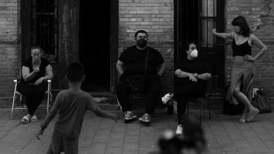 Calle de Los Angeles still. People sit on folding chairs in the street.