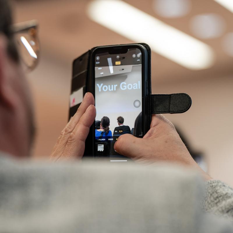 At NEXTWAVE a man takes a photo of a screen that says YOUR GOAL