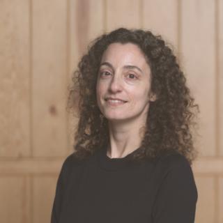 Irini Papadimitriou smiles at the camera. Irini has curly brown hair and a black top on.