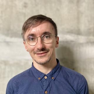 Nico Unterman smiles at the camera. He wears a blue shirt and short brown hair.