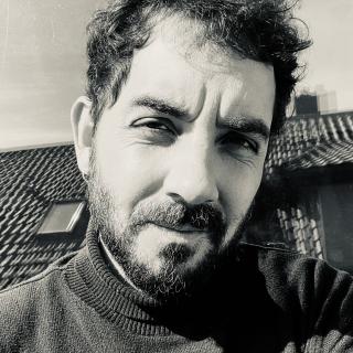Nicolás Camilo Zanetta-Colombo smiles in a black and white photo. He has dark curly hair and a beard.